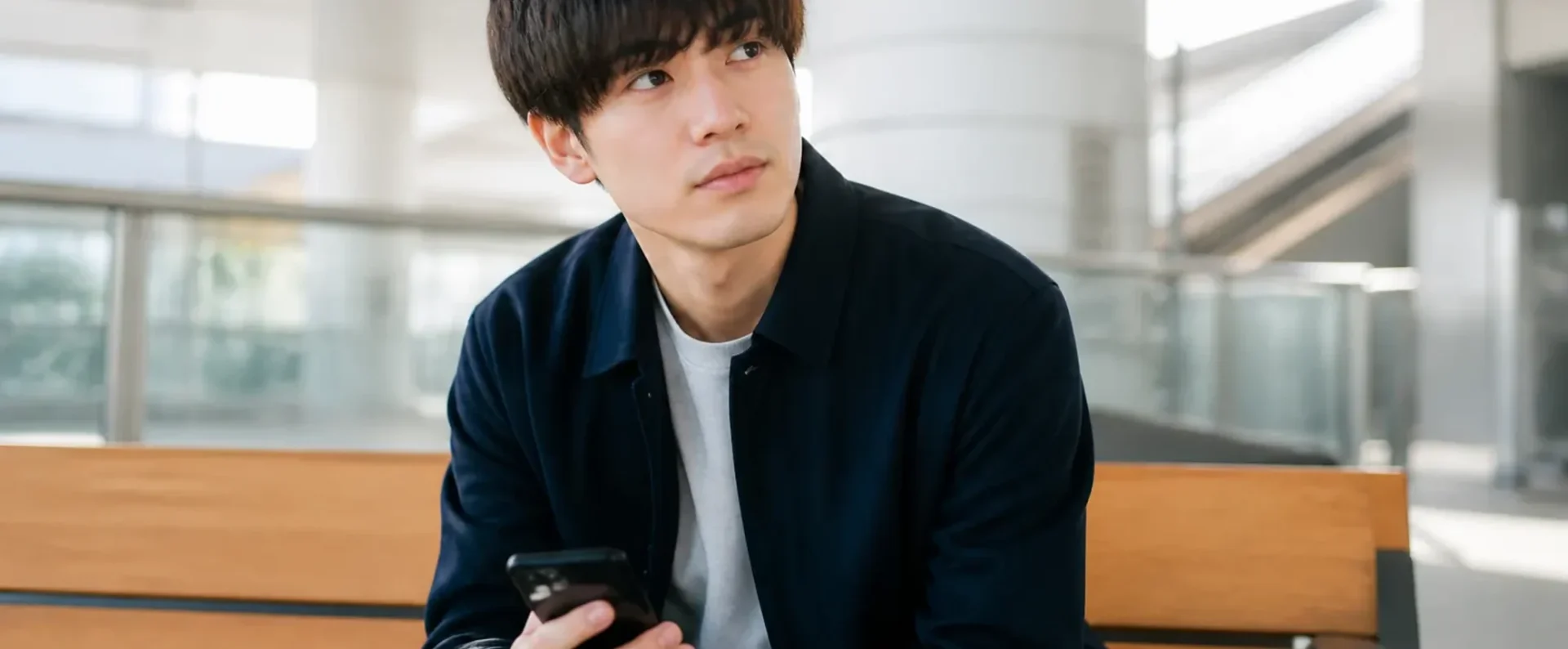 ベンチでスマートフォンの婚活アプリを見る20代男性